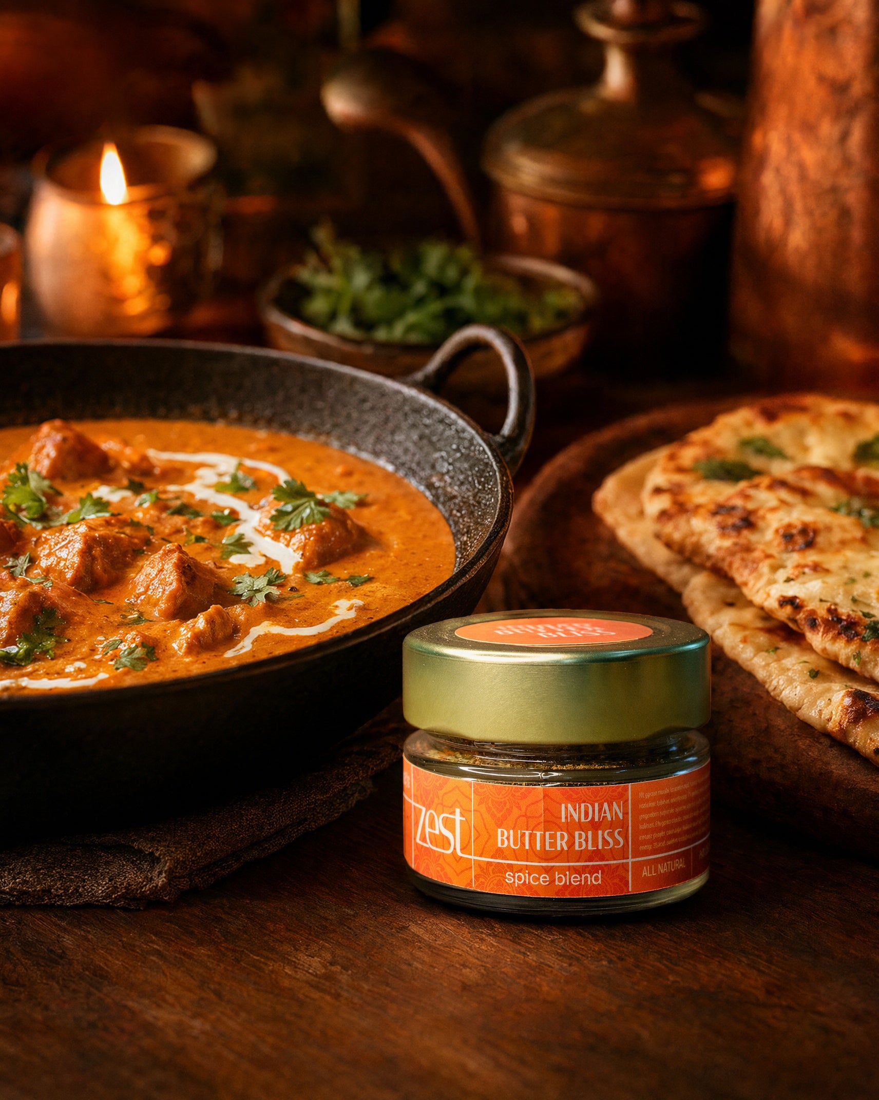 A ZEST Indian Butter Bliss spice blend jar displayed next to a rich butter chicken or paneer dish and naan bread on a dark wooden table, with candlelight in the background.