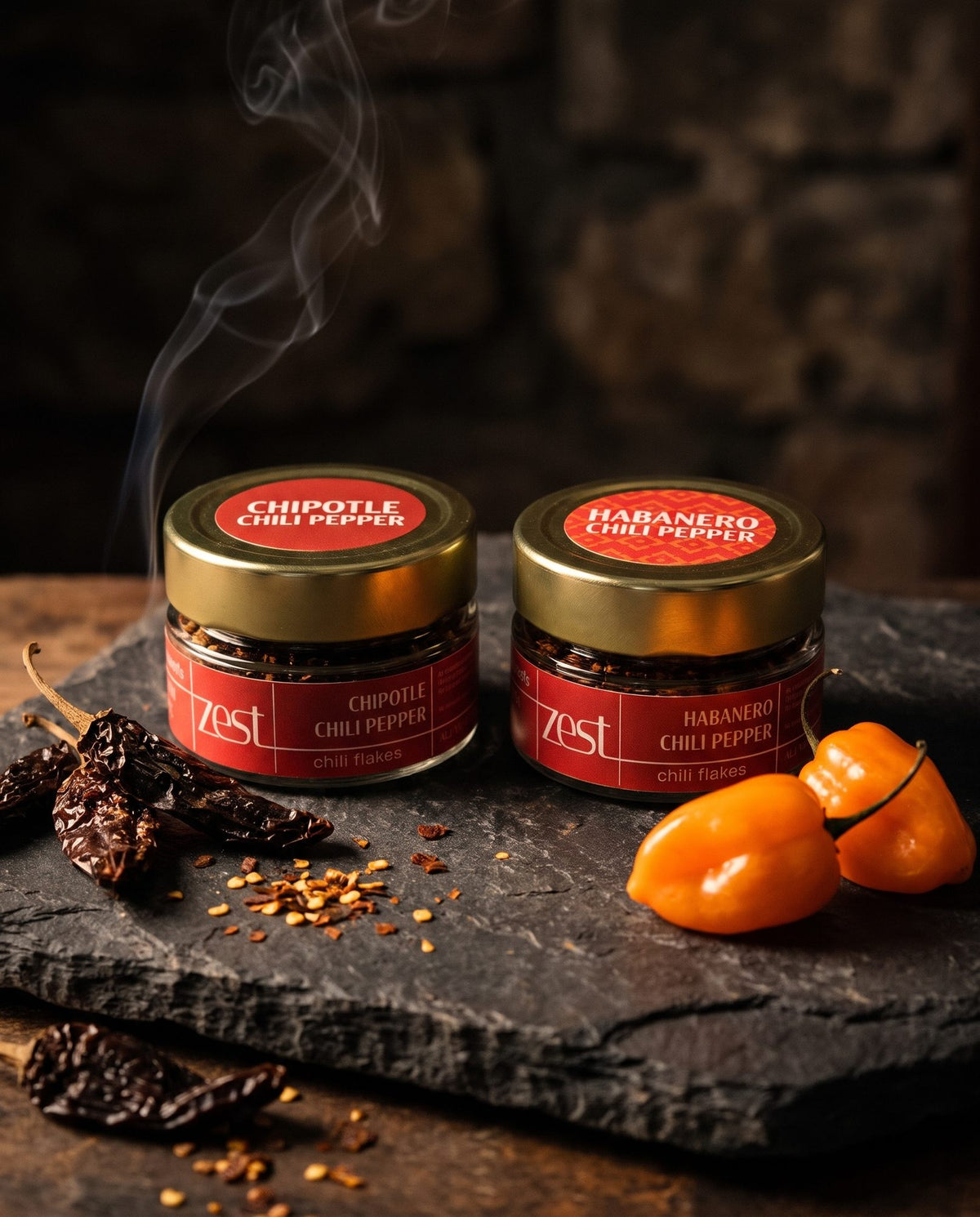 Chipotle and Habanero chili flakes jars on slate with dried chilies and smoke